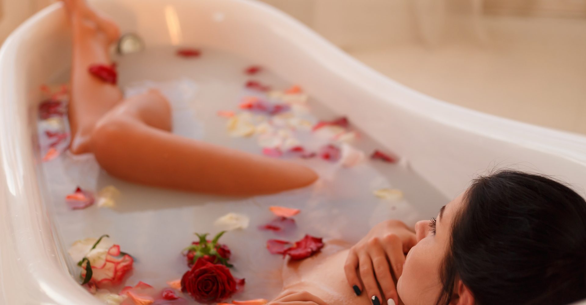 Attractive girl takes a bath with milk and rose petals. Spa treatments for skin rejuvenation